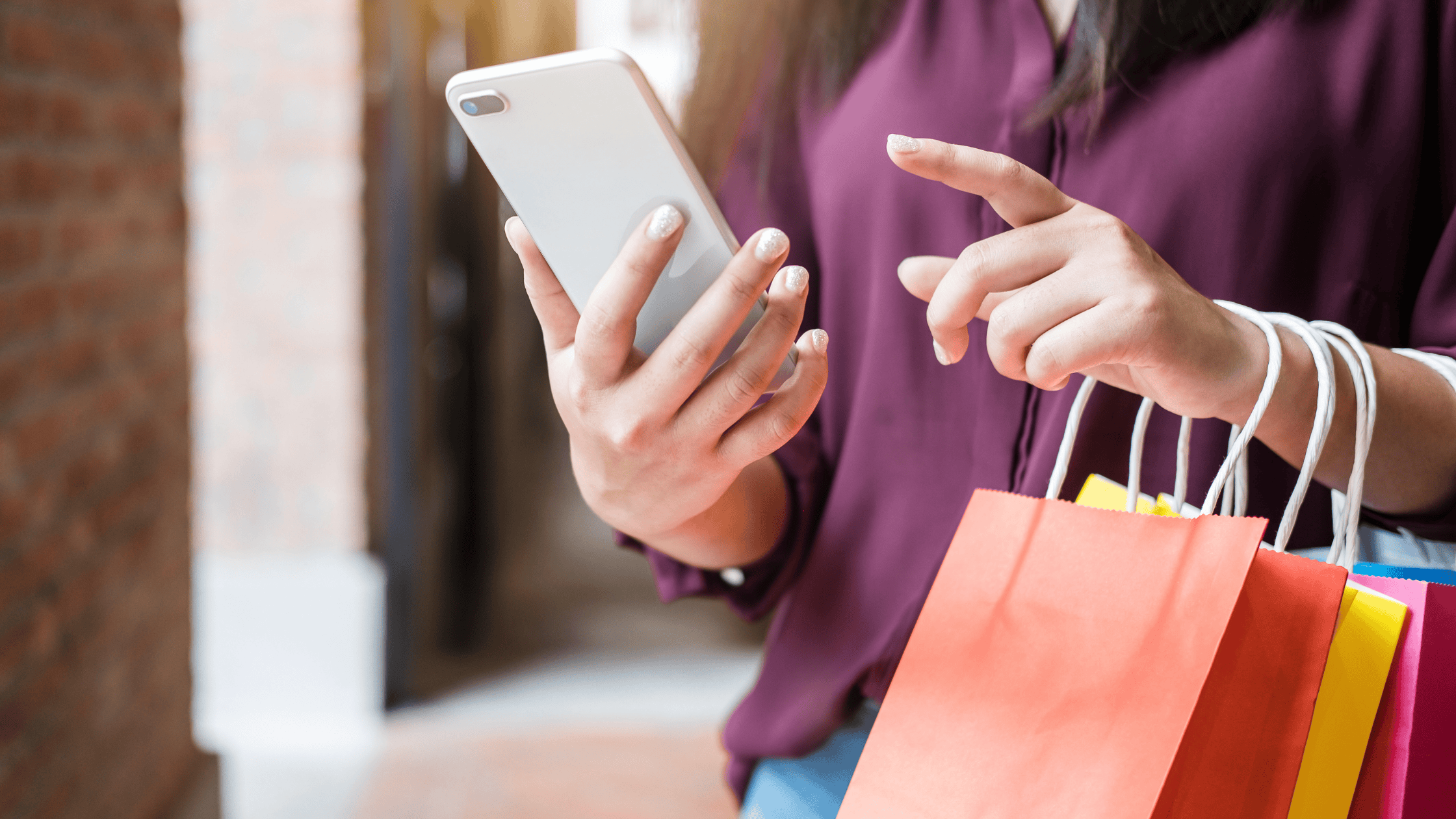 Woman holding phone, preparing to use it while shopping bags hang from her arm
