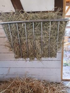 Heu in einem Edelstahl-Warntafel auf einem Bauernhof, geeignet für die Ernährung von Tieren, mit Holz und Stallumgebung im Hintergrund.