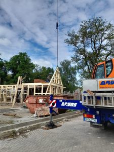 Holzbau im Bauprozess, Baukran hebt Holzrahmen für nachhaltiges Wellnesshof-Projekt in der Natur.