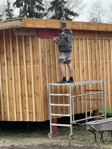 Handwerker beim Bau eines Holzhauses auf dem Wellnesshof RaJa, Holzbau, nachhaltiges Wohnen, Naturverbundenheit, ländliche Atmosphäre, ökologische Baumethoden, Handarbeit, Umweltbewusstsein, Projekte im Grünen, Holzverarbeitung, Naturmaterialien, Wellnesshof RaJa, ökologischer Holzbau, nachhaltiges Bauprojekt, ökologische Bauweise, idyllisches Grundstück, ökologische Bauweise, Handwerkskunst, Natur pur.