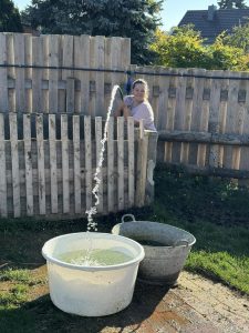 Besucher beim Wasserholen im privaten Garten am Wellnesshof RaJa, entspanntes Ambiente, Natur, nachhaltige Erholung, ländliche Idylle, Wellness und Naturerlebnis in Deutschland.