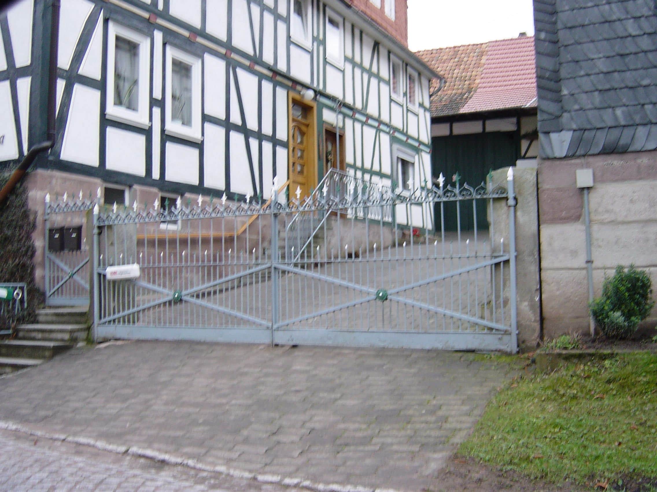 Massives graues Metalltor von Tore & Torsysteme von Stahl- und Metallbau Drost vor einem traditionellen Fachwerkhaus.