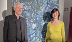 Fortunat Frölich und Myriam Thyes vor dem Gemälde ‚Hommage an Mandelbrot No. 11 – Skywalk‘ des Malers Otto W. Liesch. Theater Chur, 4. April 2025