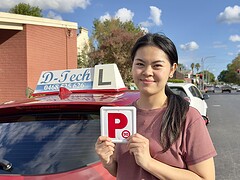 Happy student holding new P-plates after passing their practical driving exam.