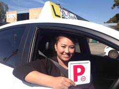 Happy student holding new P-plates after passing their practical driving exam.
