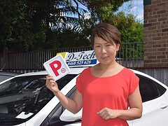 Successful student in a red top holding her red P-plate outside the D-Tech dual-control instructor car after passing her test.