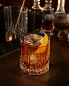 Rocks bardakta büyük buz ve limon kabuğuyla servis edilen amber renkli Vieux Carré kokteyli