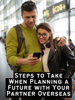 A young couple standing in a bright airport terminal, smiling while looking at a smartphone together, representing the planning phase of travel.