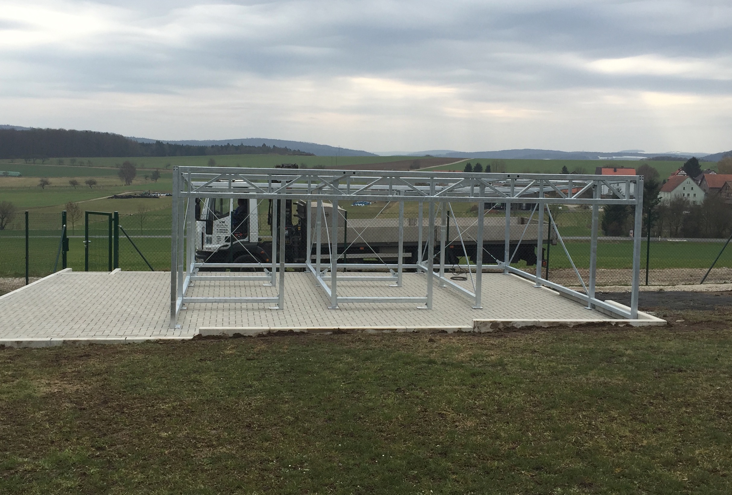 Robuste verzinkte Stahlrahmenkonstruktion von Stahl- und Metallbau Drost auf gepflastertem Untergrund, ideal für Carports oder Überdachungen, in ländlicher Umgebung mit Feldern und Hügeln.