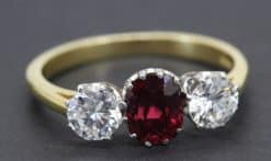 Gold ring with central ruby and two side diamonds, fine jewelry piece.
