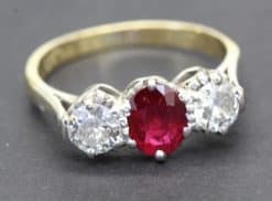 Ruby and diamond engagement ring with a central oval ruby flanked by two diamonds.