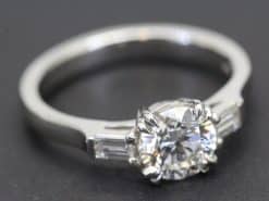 Elegant diamond engagement ring with a central round cut stone and baguette side stones.