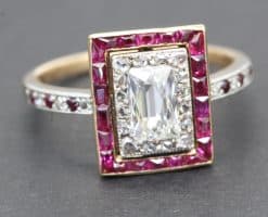 Elegant diamond ring featuring an emerald-cut center stone surrounded by pink gemstones and a diamon.