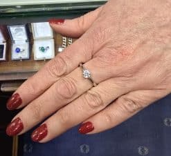 Diamond engagement ring on woman's hand with red nail polish.