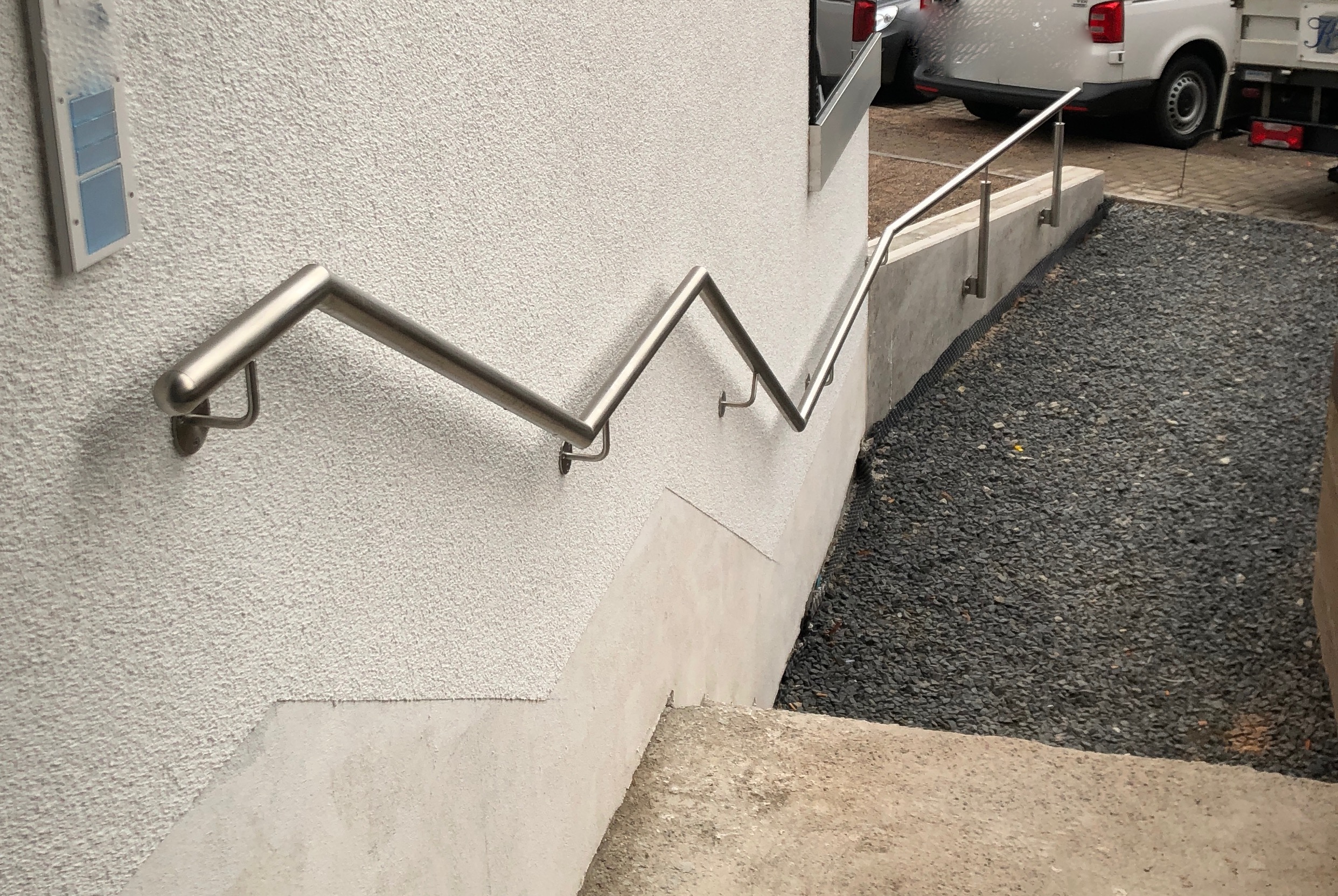 Edelstahlhandlauf von Stahl- und Metallbau Drost an einer Außentreppe, montiert an einer weißen Putzwand.