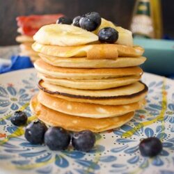 Stack of american pancakes topped with bananas, blueberries and syrup.