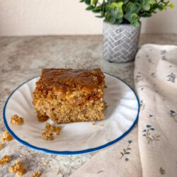 apple cake on plate on top of a neutral colored kitchen counter with a floral kitchen towel next to it