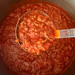 How to Make Spaghetti Sauce Thicker. Pot of homemade spaghetti sauce simmering on the stove, with a ladle lifting a spoonful to show its thick, rich texture with tomatoes and herbs.