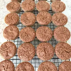 1 dozen chocolate zucchini muffins cooling on a wire baking rack on a neutral colored kitchen counter.