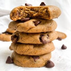 A stack of 5 protein cookies with chocolate chips, the top cookie has a bite taken out