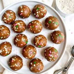 above shot of edible cookie dough balls with sprinkles on a white plate next to cookie scooper