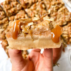holding a salted caramel apple pie bar with the rest in the background