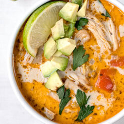 top shot of white chicken chili in a white bowl topped with a lime and avocado
