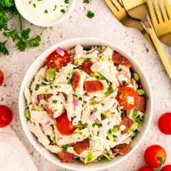A bowl of BLT chicken salad next to forks and dressing.