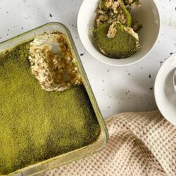 matcha tiramisu in a dish, plates with slices on the side and a napkin, from above