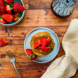 pancakes on a blue plate with strawberries on top, napkin and fork on the side, wooden background