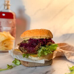 oyster mushroom burger on a wood board, salad aroun, in the background a striped towel, crisps and a bottle of bitter, on a marble background