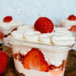 mini strawberry cake pots with strawberries around, on a wooden board, speckled background