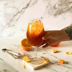 hand reaching for aperol spritz mocktail, marble background, ice tongues and slices of orange around