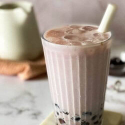 taro latte in a glass with a straw, on a marble coaster, jug, towel and boba pearls in the background, on a marble background