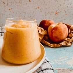 peach curd in a jar on a plate, under a towel, in the back two peaches on a paper bag