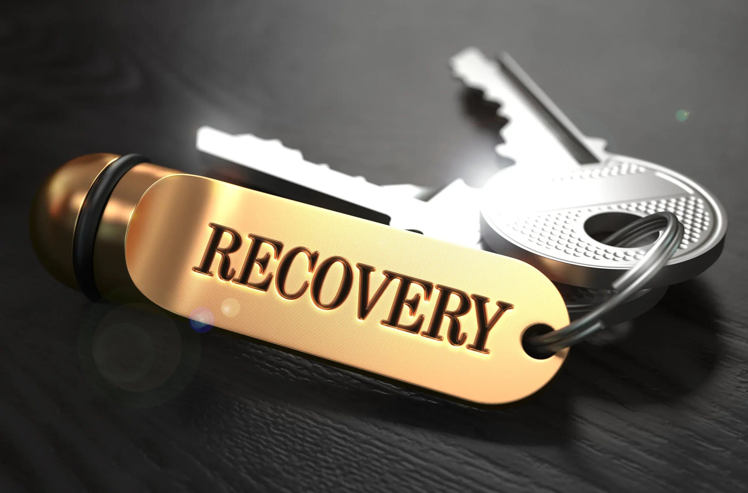 Close-up of a gold tag reading 'RECOVERY' attached to a key ring with a silver key in the background.