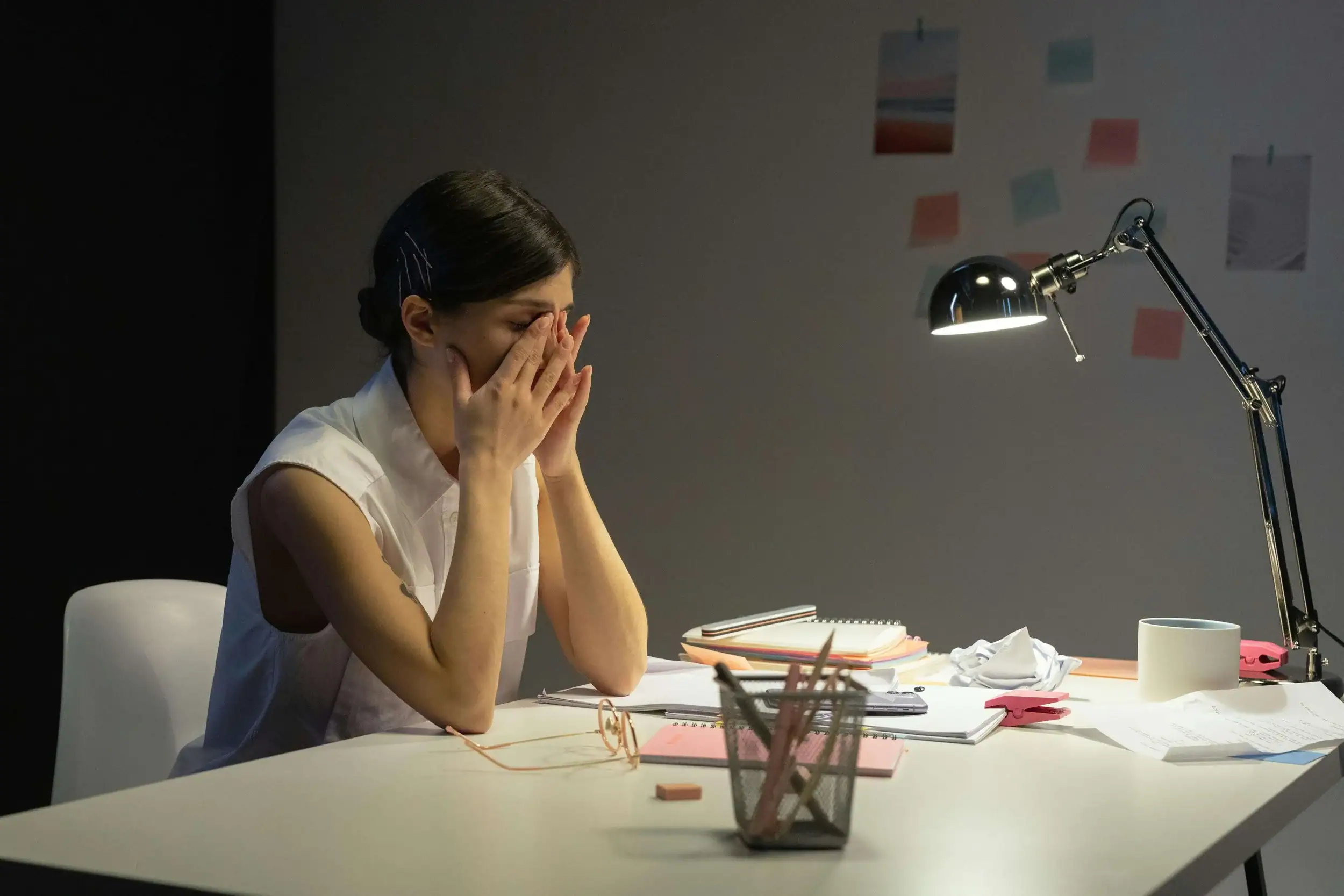 Woman stressed at her desk, resting her head in her hands who would benefit from somatic therapy in Michigan and guided by a somatic therapist in Detroit for burnout recovery and nervous system regulation.