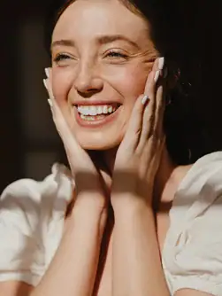 Woman holds her smiling face. Looking into starting therapy for empaths in Michigan? Our caring empath counselors in Detroit can assist you today!