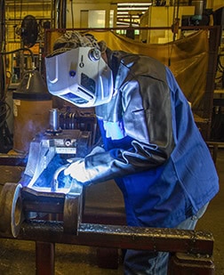 Welder leaning over project in a weld cell