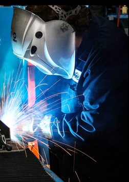 Side view of welding operator welding part with sparks flying