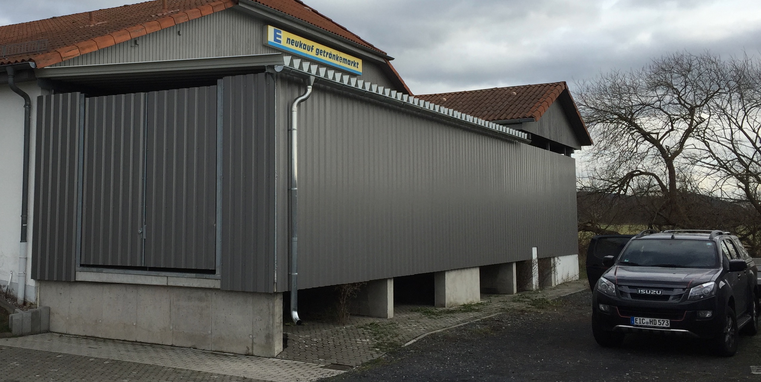 Ansicht der dunkelgrauen Trapezblechfassade am E neukauf Getränkemarkt, fachmännisch montiert von Stahlbau von Stahl- und Metallbau Drost, mit sichtbarer Regenrinne und Fallrohr.