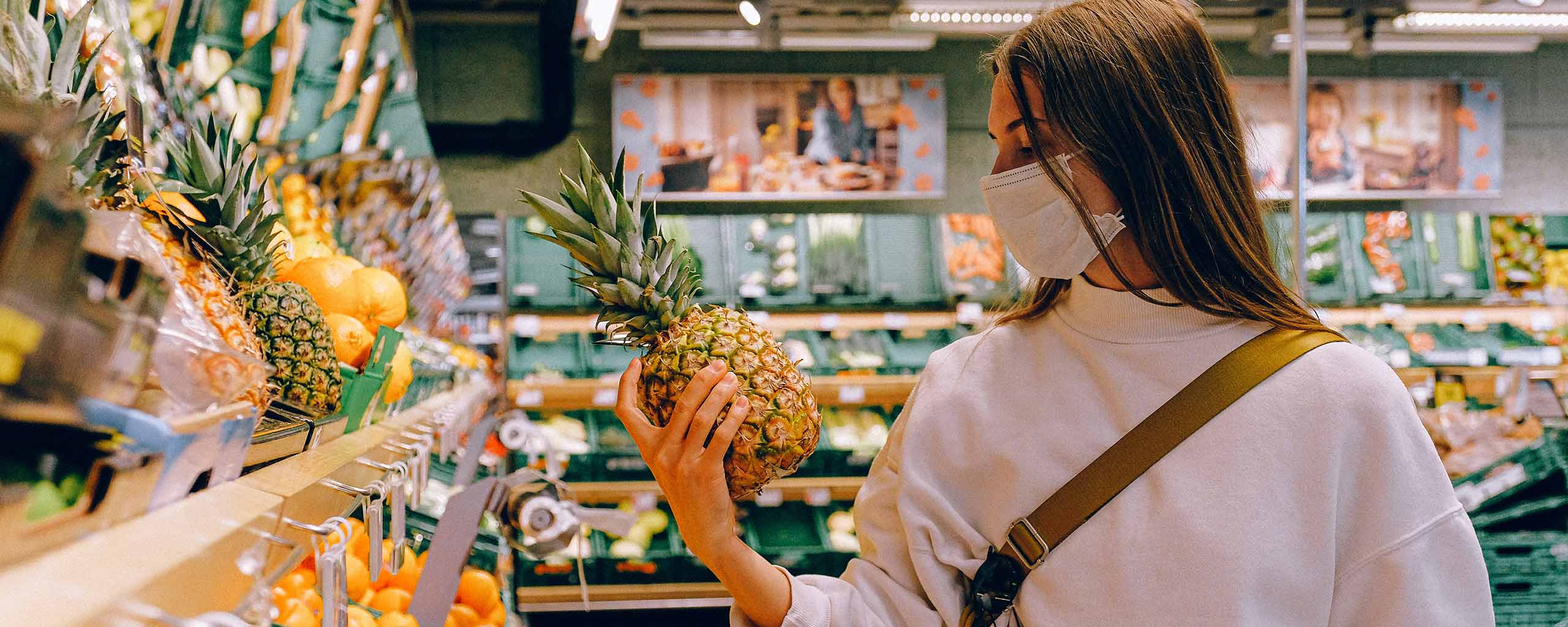 Woman shopping at the grocery store wearing a facemask and holding a pineapple