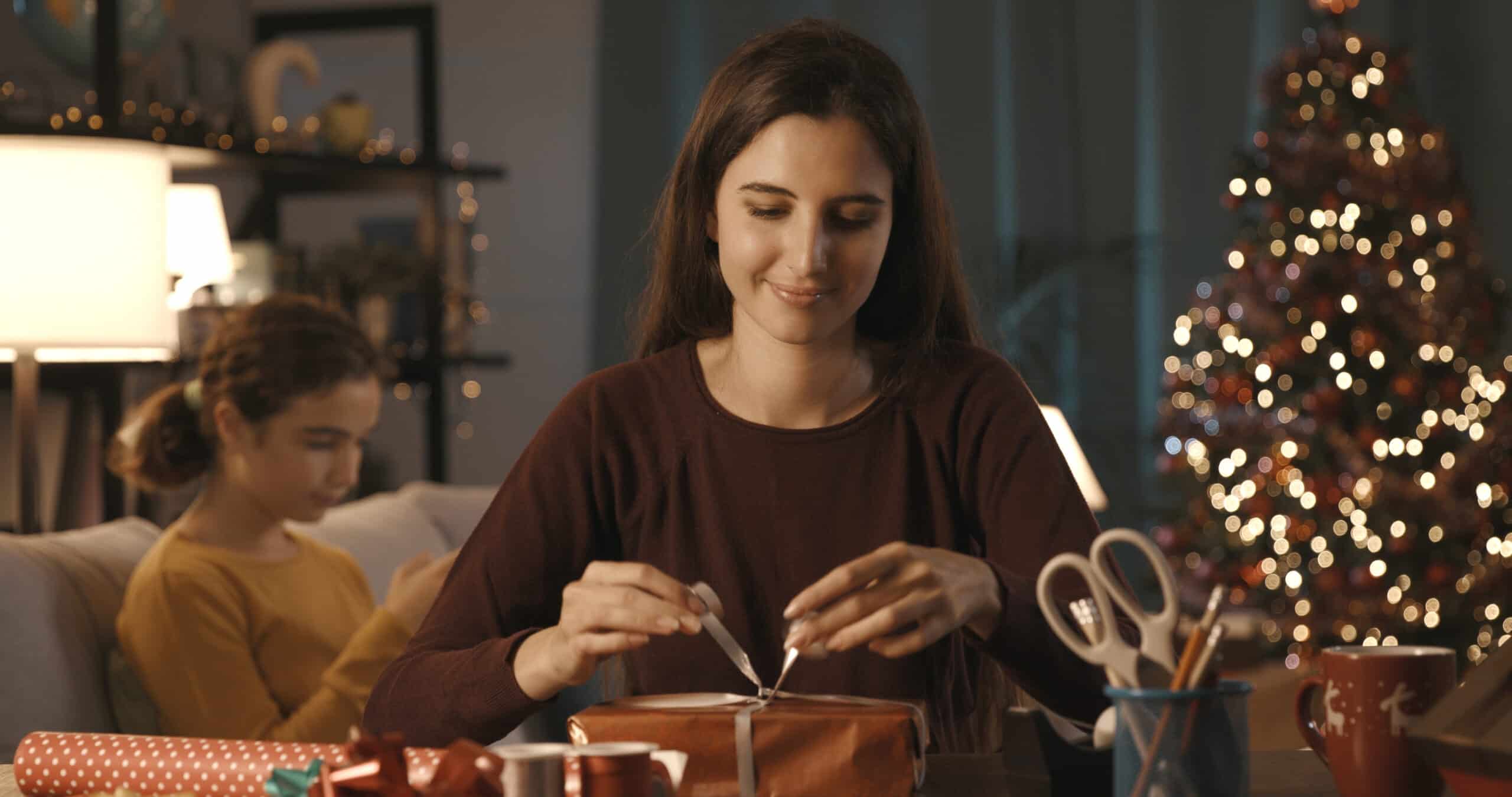 Woman preparing Christmas gifts at home, her sister is sitting in the background