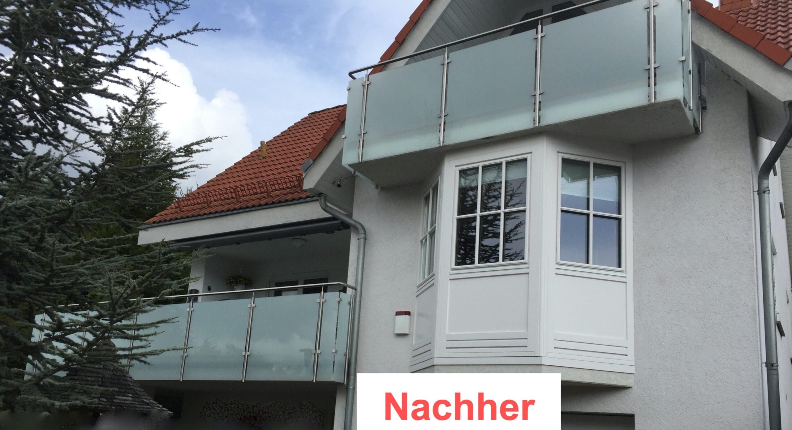 Zwei moderne Balkone von Stahl- und Metallbau Drost mit Milchglasgeländer und Edelstahlpfosten an einem weißen Haus mit rotem Dach, nach der Sanierung.