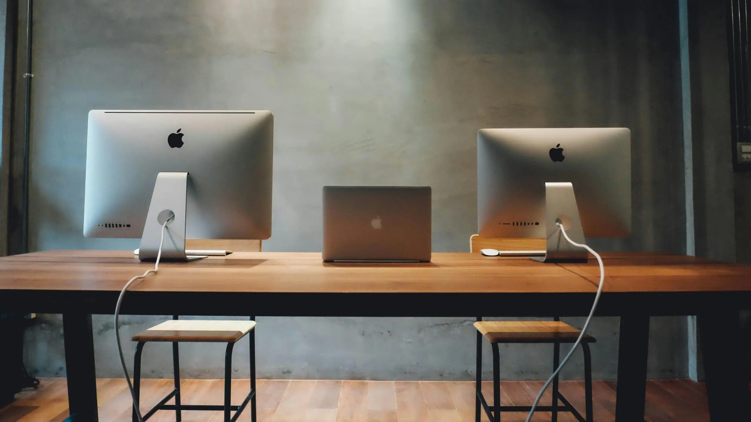 A photo of an office with two iMac computers and a macbook in the middle of the desk.