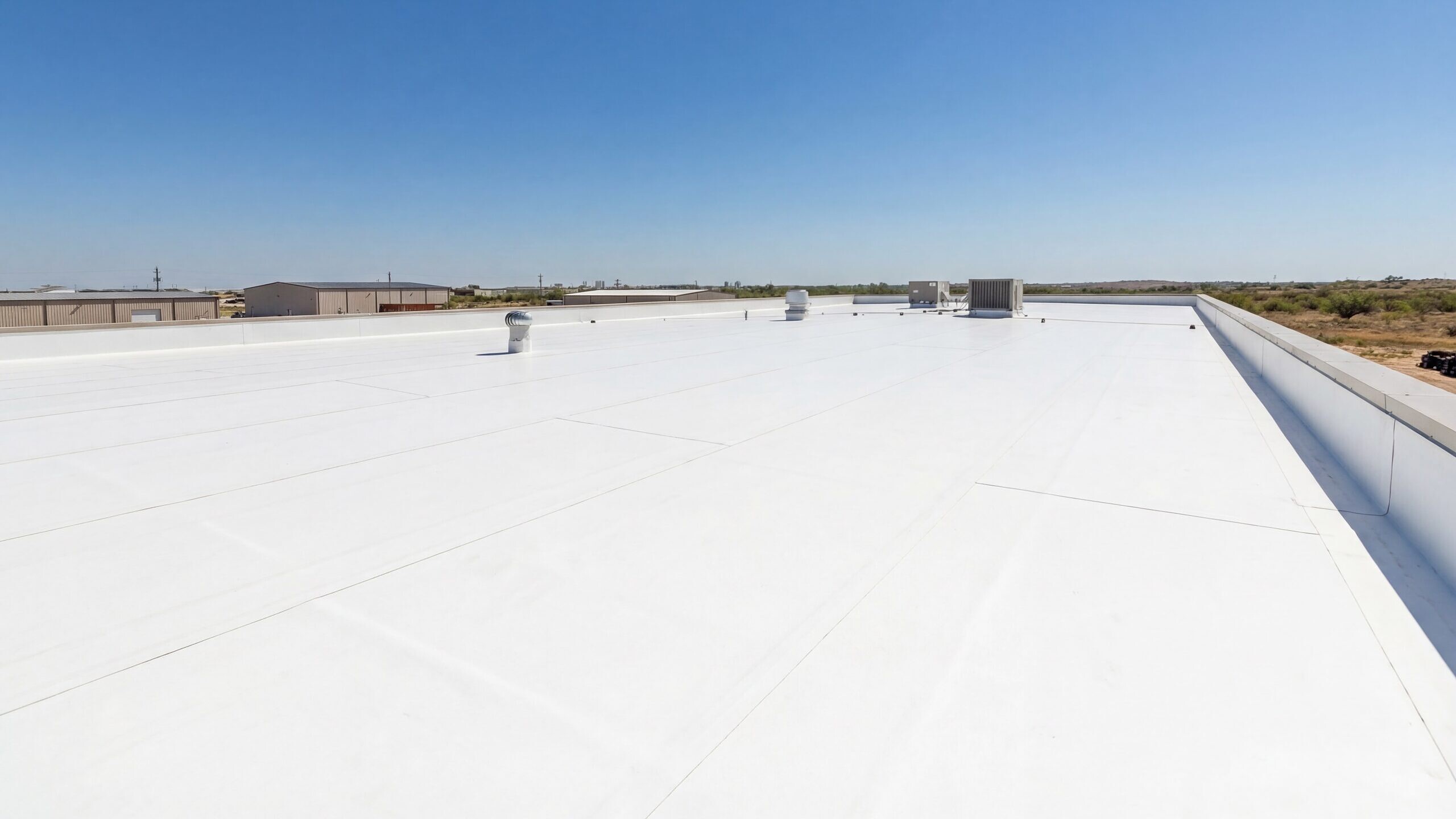 Flat white commercial roof with rooftop vents under a clear blue sky