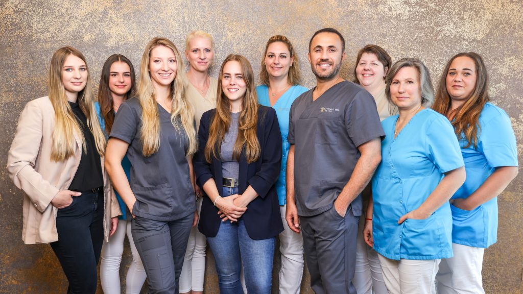 Gruppe von medizinischem Personal in professioneller Kleidung vor grauer Wand.