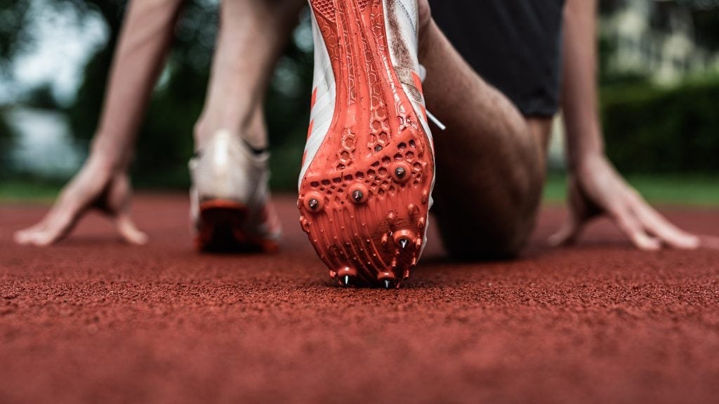 Nahaufnahme eines Sprints auf der Laufbahn, Fokus auf den Schuh und den Startblock.