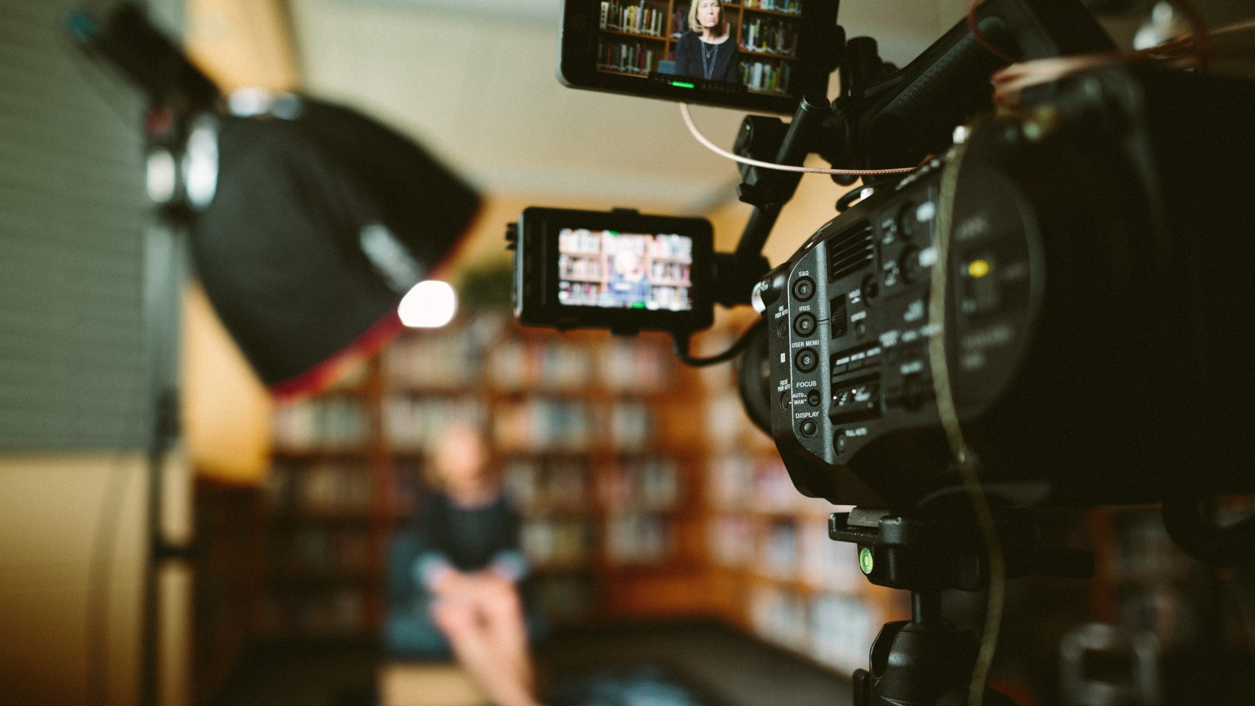 Tech Sales 01 Image shows a camera filming a sit-down video of someone surrounded by lighting and bookshelves