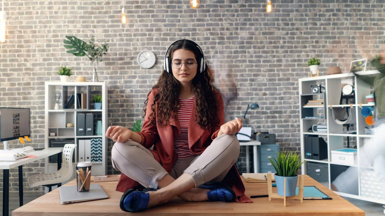 Young woman meditating with headphones in a modern office setting, practicing mindfulness.